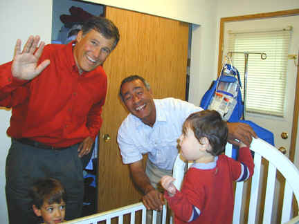 Inslee waving for the camera, behind toddler's play pen with Maher Shebl. Ahmed Shebl, inside pen, facing Inslee.