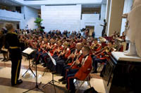 uniform band members playing, seated in semi-circle among the statues on the floor of large marble floor exhibition space