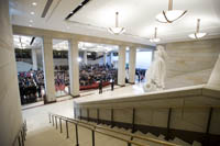 view from above, back and side of 19 foot white statue of a robed woman overlooking large audience in exhibition space