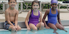 Three kids at a pool ready for swimming lessons