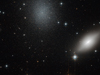 Background stars burn from behind an almond-shaped blurry white galaxy and a diffuse speckled glob of stars