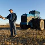 Two men shaking hands in front of a tractor.