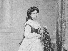 Black and white portrait of Vinnie Ream standing in a dress behind a chair.