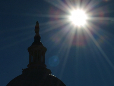 Bright sun behind a silhouetted Capitol Dome and Statue of Freedom.