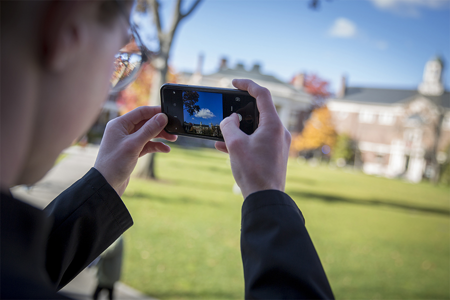 Student taking a photo with his phone outside on Harvard' campus