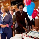 Congresswoman Pelosi standing at a table next to a cake