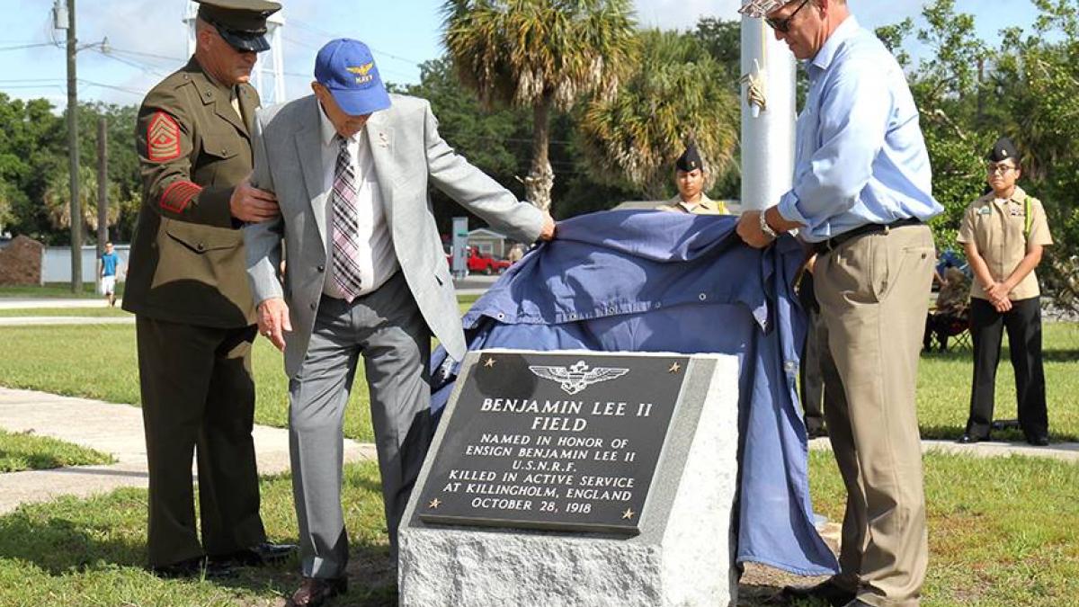 Retired Lt Cdr. Joe Elliott helps US Representative Ted Yoho unveil a plaque rededicating the field to Ensign Benjamin Lee II, U.S.N.R.F.