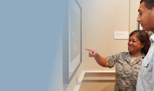 A woman in uniform points to a painting on the wall, another observer stands by.