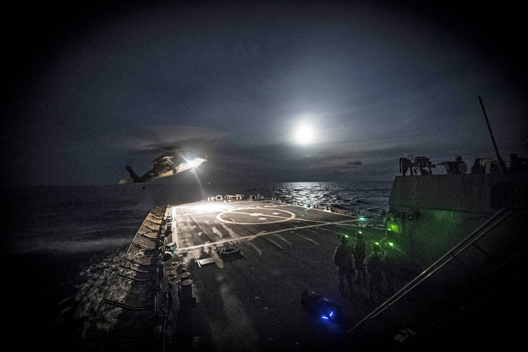 A helicopter lands on a ship at night.