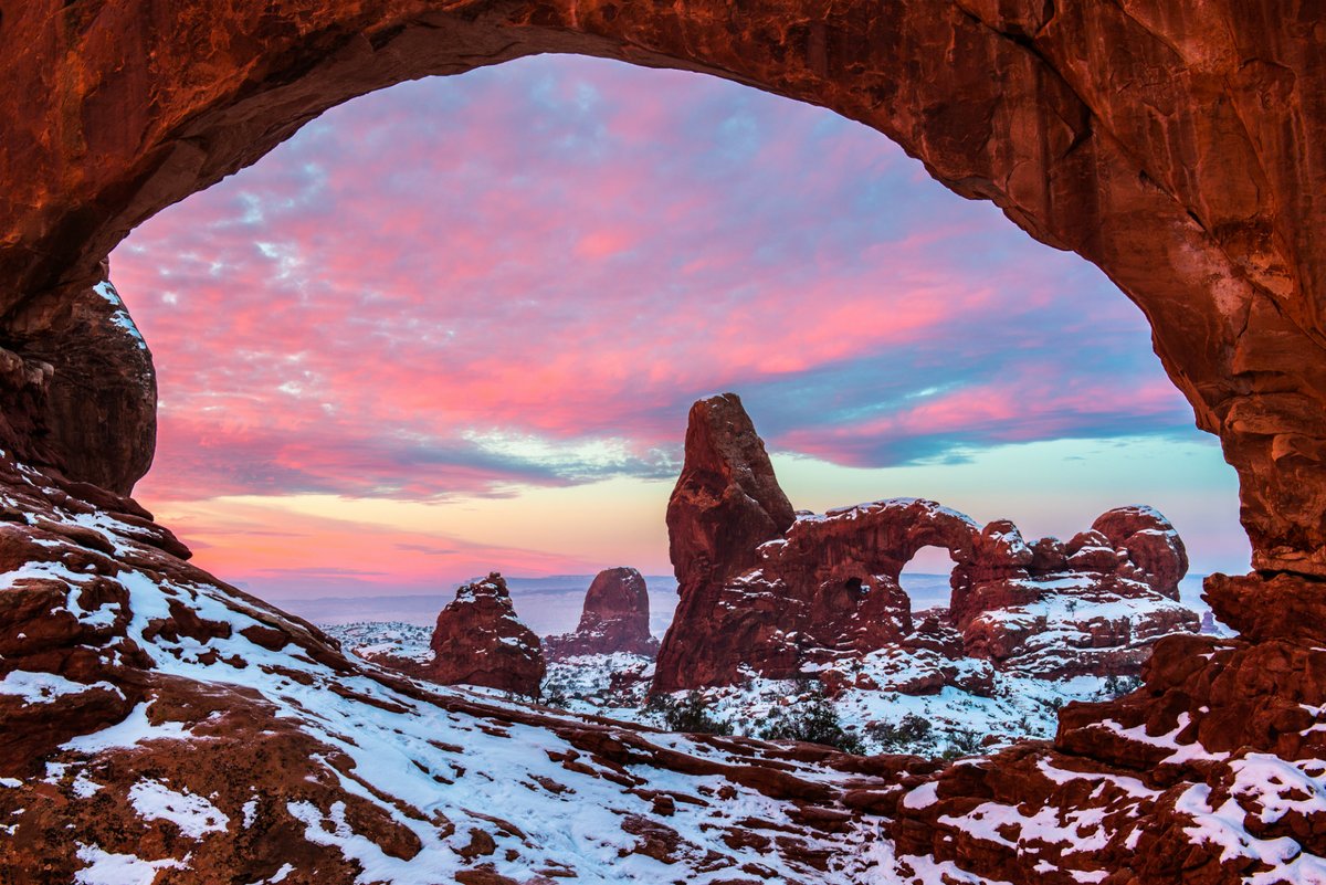 A view of rounded red rock formations dusted with snow under a pink sunset sky.