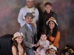 A Hispanic man and woman with their two daughters and three relative foster children. They are sitting and smiling at the camera.