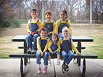 Six Caucasian children. Three boys and three girls sitting on a picnic table smiling at the camera. 