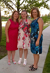 Two Caucasian women with their Caucasian foster daughter. They are standing and smiling at the camera. 