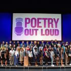 Students stand on risers on a stage with a Poetry Out Loud sign behind them.
