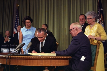 President Lyndon Johnson signs the Medicare Bill. President Harry S. Truman is seated next to him. Others looking on include Lady Bird Johnson, Vice President Hubert Humphrey, and Bess Truman. July 30, 1965. Photo courtesy of Lyndon B. Johnson Presidential Library, U.S. National Archives