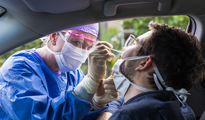 Health care worker administering COVID-19 test to a person setting in a car.