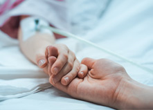 An adult holding the hand of a child who is hospitalized.