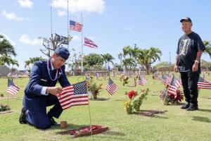 Pictured Vietnam Veteran Ed Kawamura watches as Congressman Kai Kahele adjusts the American flag at the grave of Clyde Caires