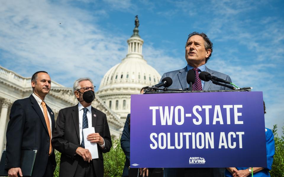 Congressman Andy Levin at a podium in front of the US Capitol Building with a purple sign with white letters that reads the Two-State Solution Act