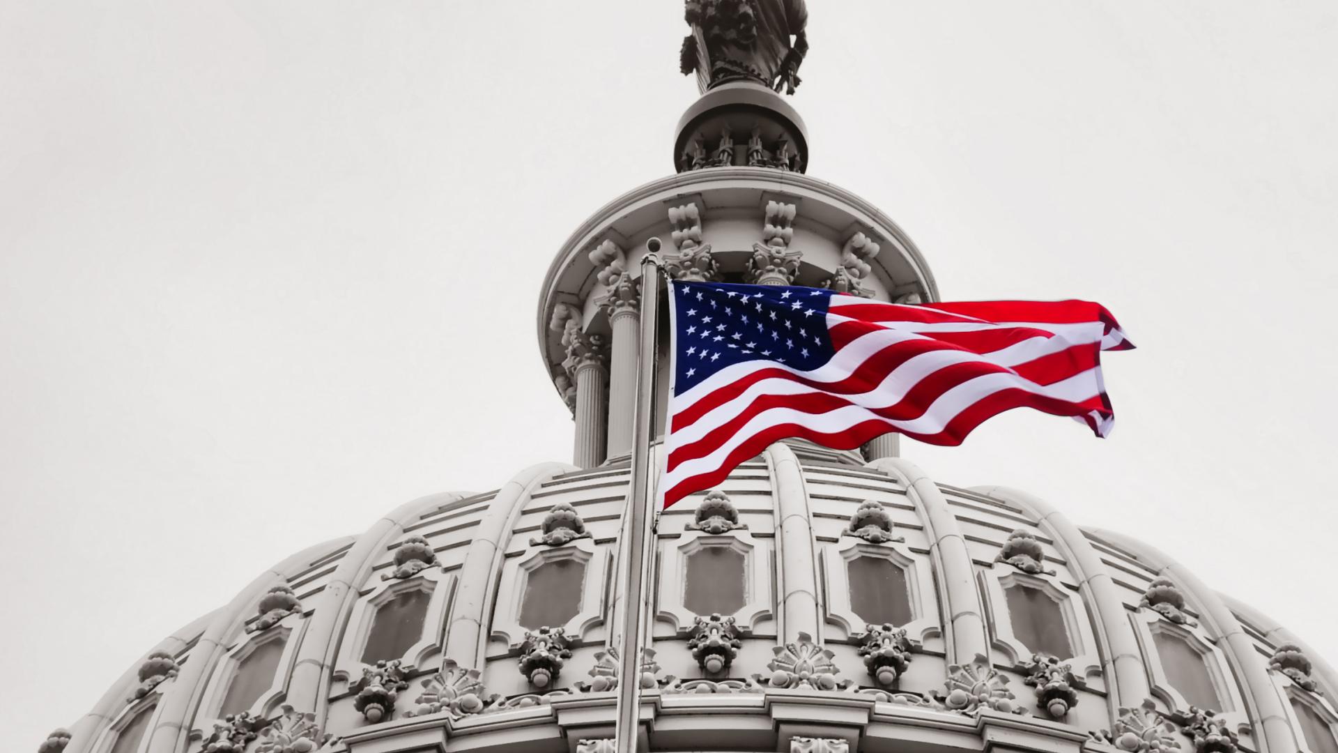 Image of the US Capitol dome with a US flag in the foreground