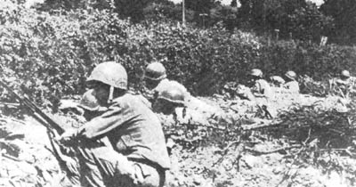 Infantrymen crouching behind bushes atop a hedgerow