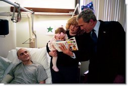 President George W. Bush reads a baby book with U.S. Army Reservist First Lieutenant Brandan Mueller of Webster Groves, Mo., his wife Amanda, and their daughter Abigail at Walter Reed Army Medical Center in Washington, D.C., Friday, March 19, 2004. Lt. Mueller was injured while serving in Operation Iraqi Freedom. White House photo by Eric Draper.
